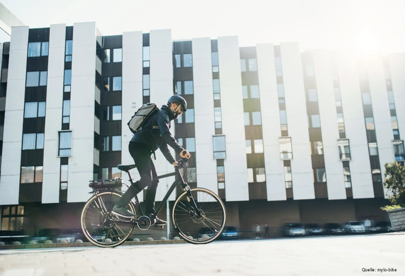 Mann balanciert vor einem Hochhaus auf einem E-Bike.