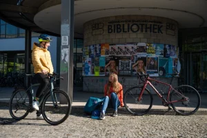 Eine junge Frau und ein junger Mann auf dem Fahrrad vor der Uni-Bibliothek.