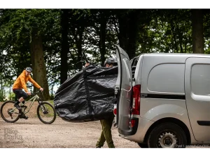 Ein Mann verlädt ein dreckiges Fahrrad, das in Roughsac eingepackt ist.