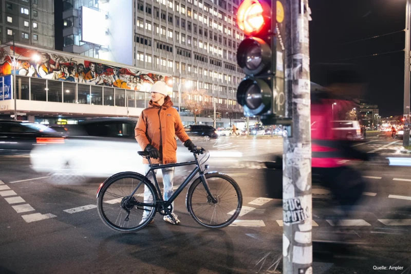 Ein Mann in Winterkleidung steht mit einem Ampler-E-Bike an einer Kreuzung.
