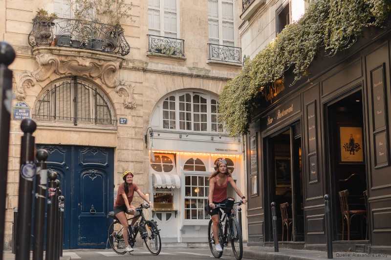 Zwei junge Frauen fahren auf Fahrrädern in den Gassen von Paris.