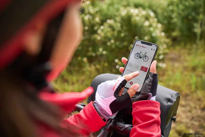 Eine Frau in Fahrradkleidung tippt auf ihr Smartphone auf dem die Brose-App geöffnet ist.
